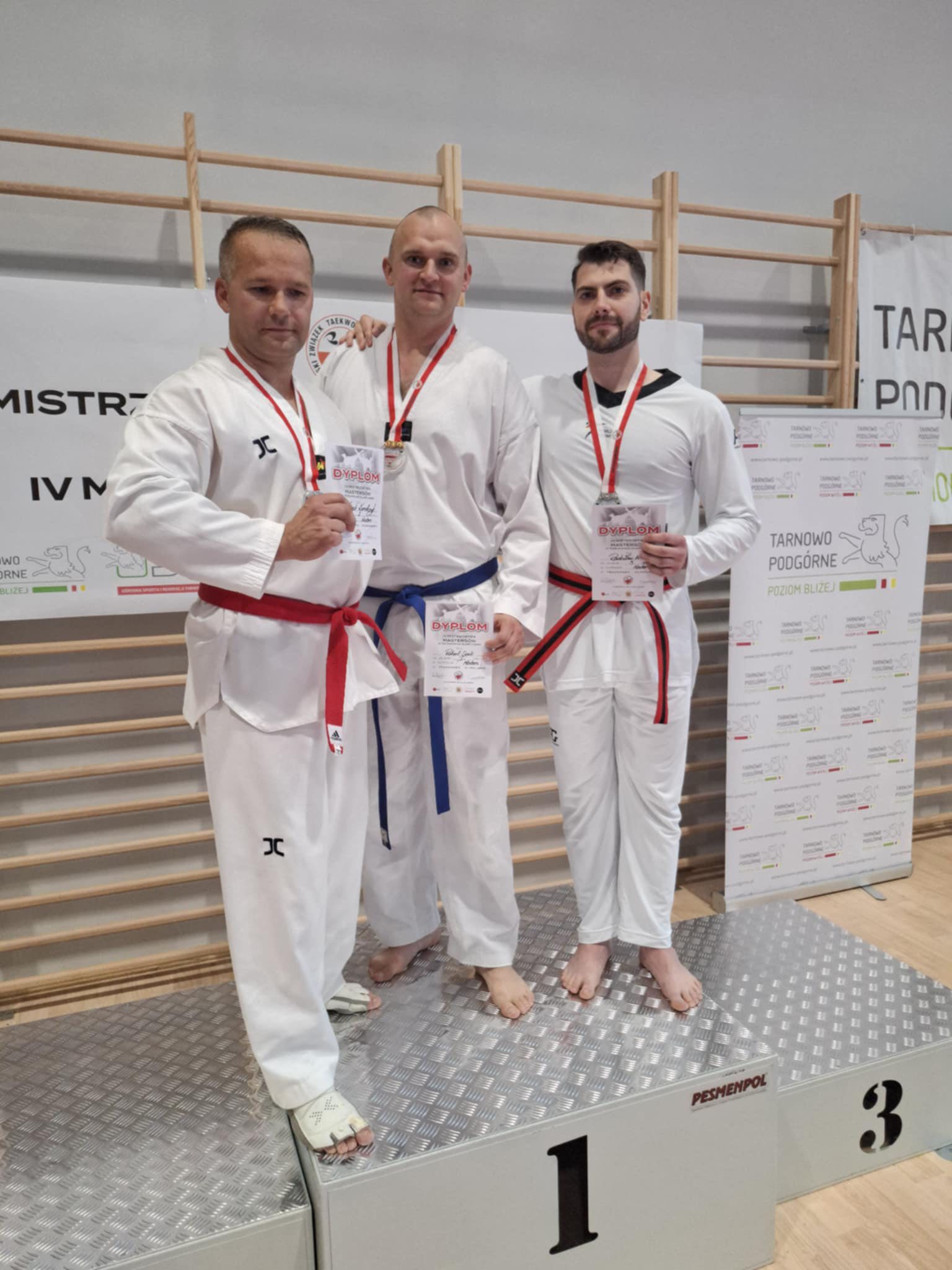 Grupa zawodników Masters w dobokach stojąca na podium.
